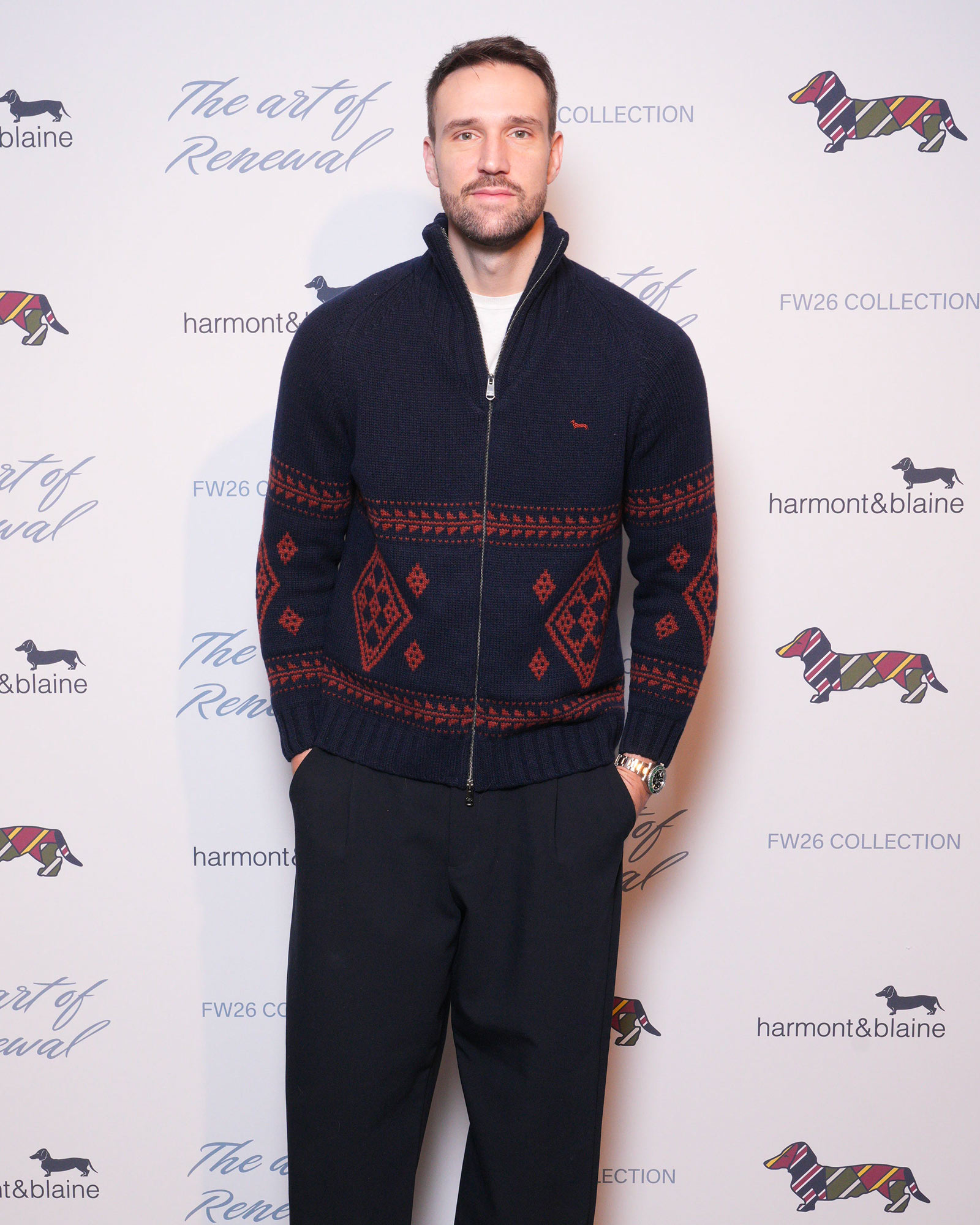 Uomo con maglione blu navy con motivi geometrici rossi e pantaloni scuri