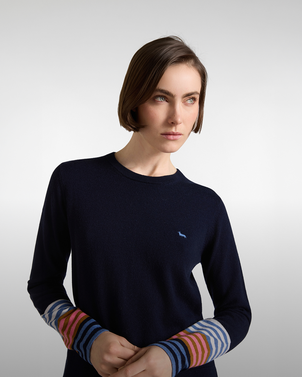 Donna con caschetto che indossa un maglione girocollo blu scuro con logo azzurro sul petto e polsini a righe multicolore.
