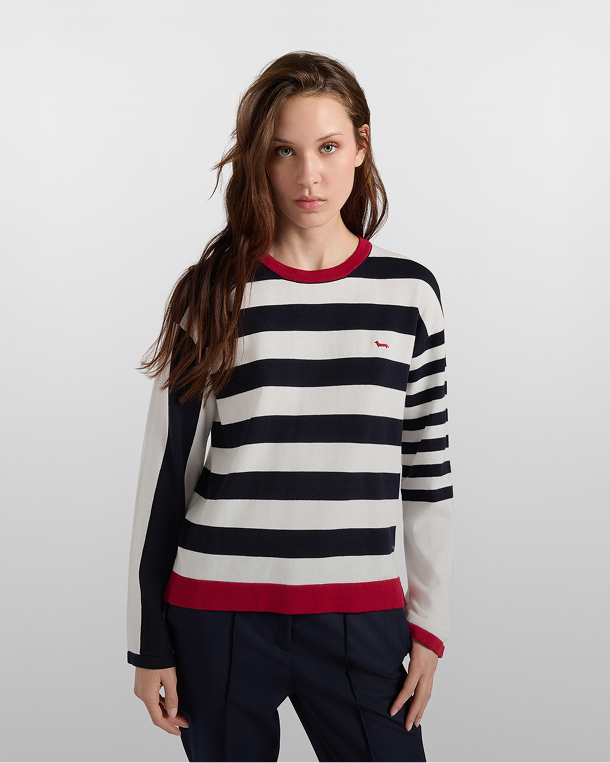 Donna che indossa un maglione a righe orizzontali bianche e blu scuro con bordi rossi e logo del bassotto ricamato sul petto, abbinato a pantaloni scuri.