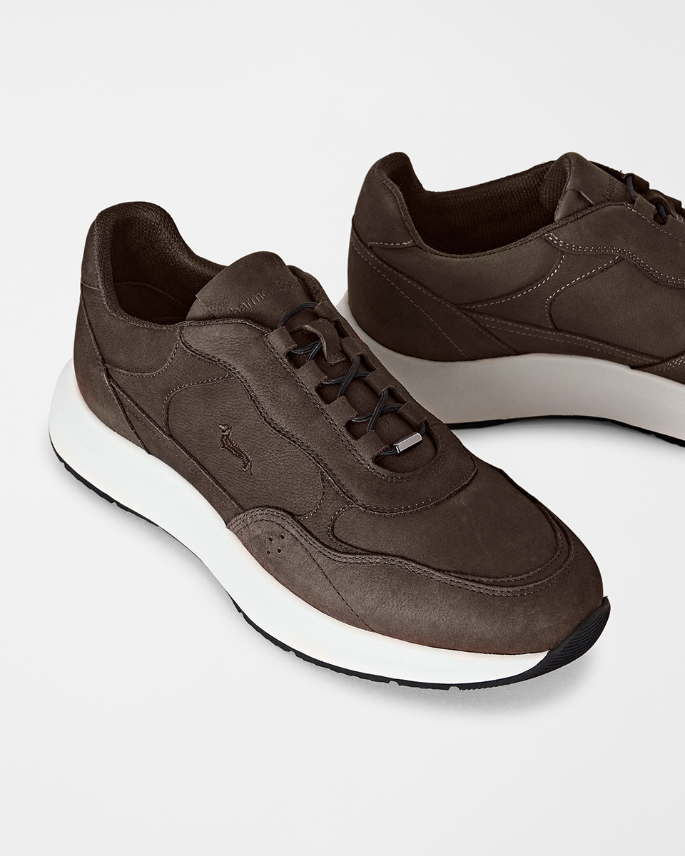 Un primo piano su uno sfondo chiaro che mostra un paio di sneaker da uomo multimateriale nei toni del blu scuro, marrone e beige, con inserti in camoscio, dettagli in mesh e suola in gomma spessa bianca e caramello.
